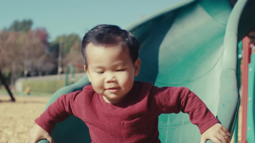 Boy accompanied by his father going down a slide in a playground