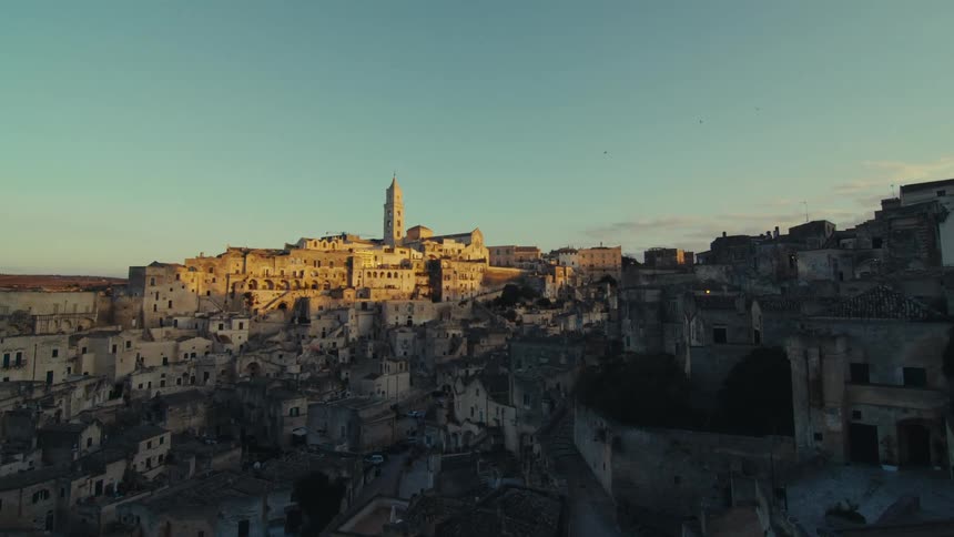 Apanoramic view of a historic town nestled on a hillside with numerous buildings constructed directly into the rock face bathed in the warm glow of the setting sun