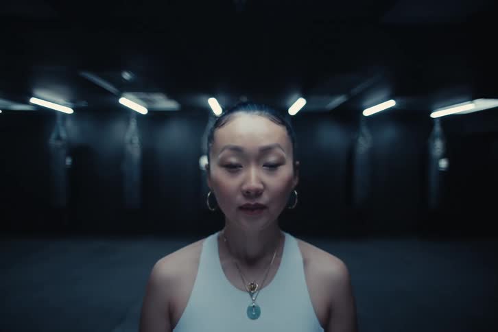 Close up of a woman standing on a dimly lit gym looking at the cameration