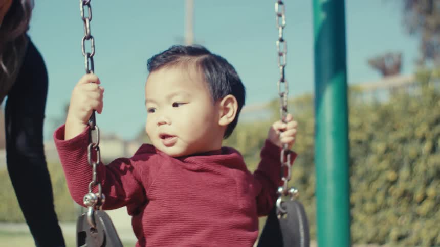 A mother pushes her son on the swing