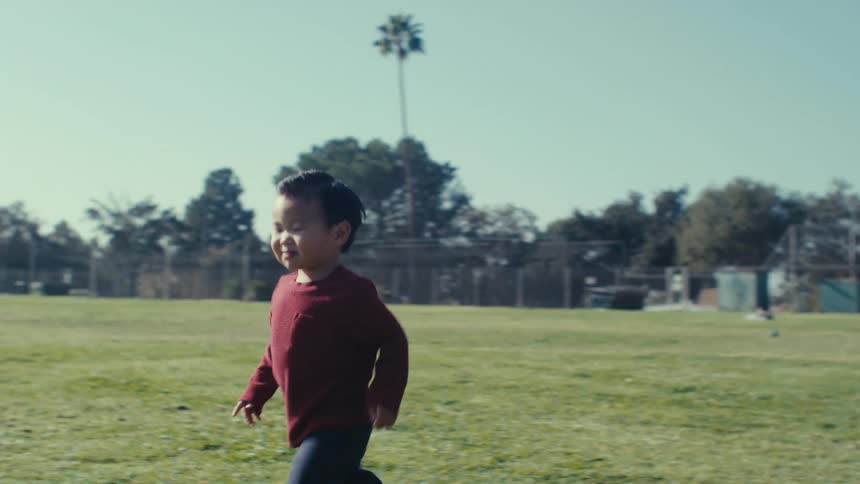 A little boy in a red shirt is walking on a green lawn on a sunny day