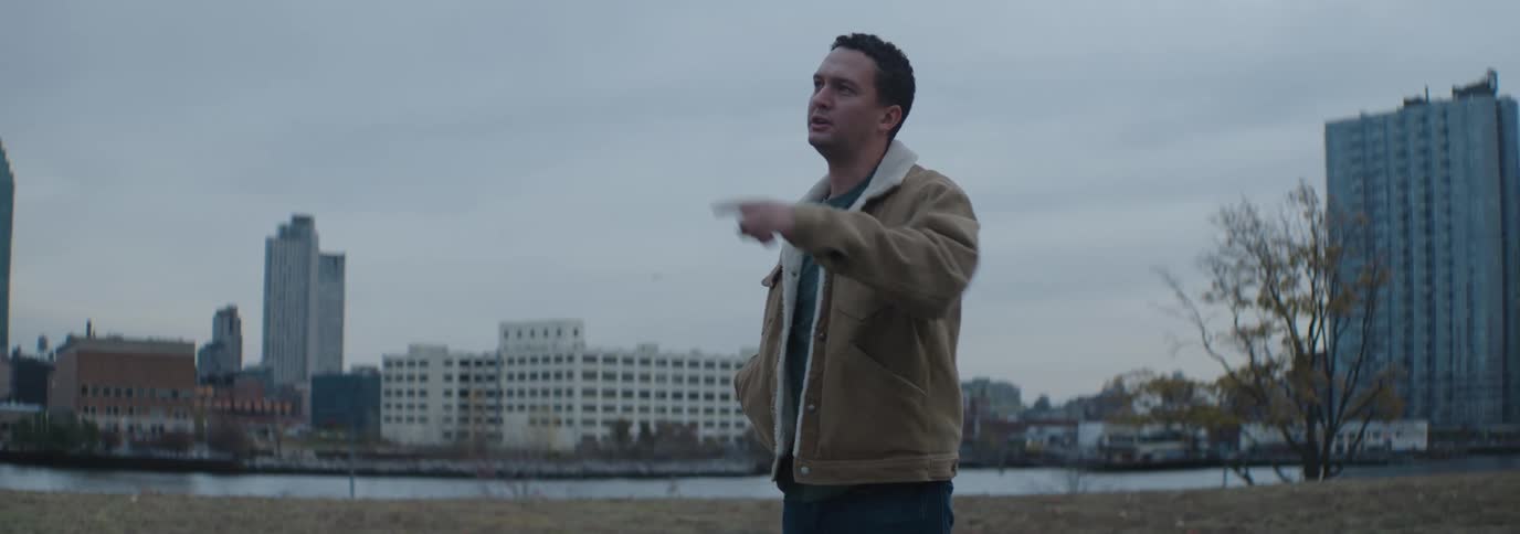 Man with a couple with suede is on the grass by a lake in a metropolis