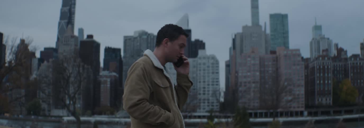 Man outdoors talking on cell phone while walking in a park with a metropolis in the background