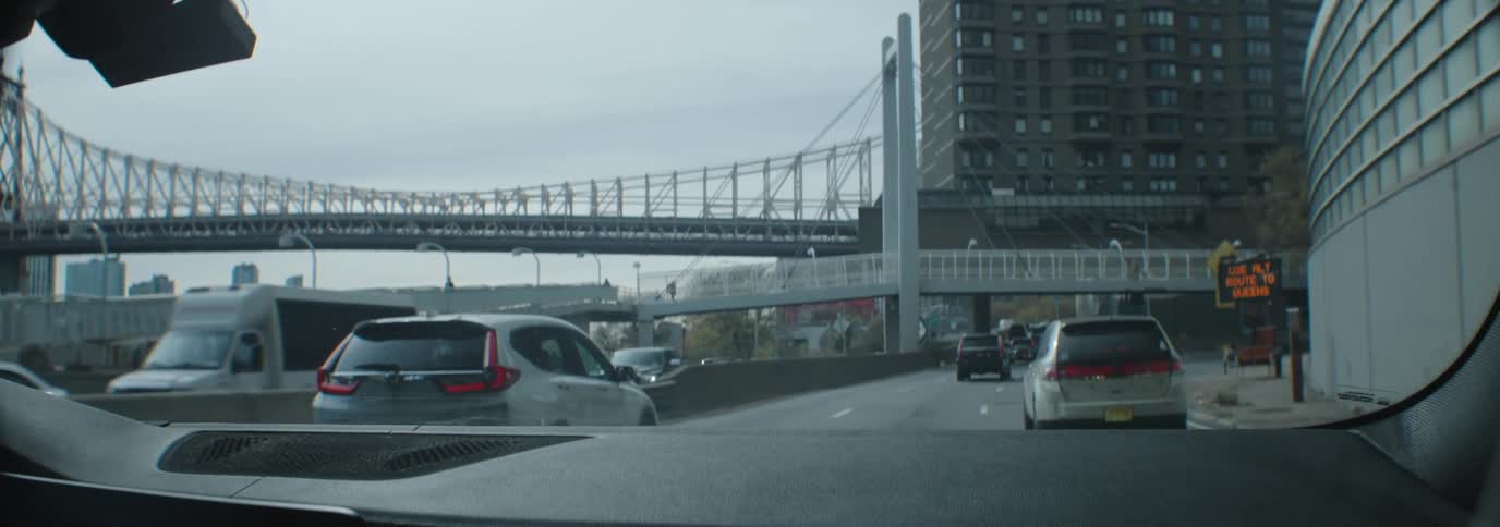 A few scattered cars drive slowly down the freeway under a bridge in the city