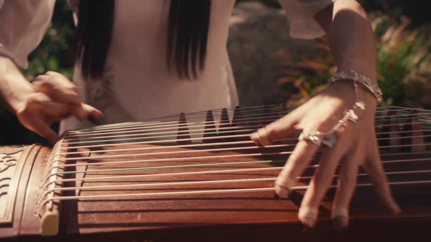Woman plays a guzheng like string instrument while in the garden