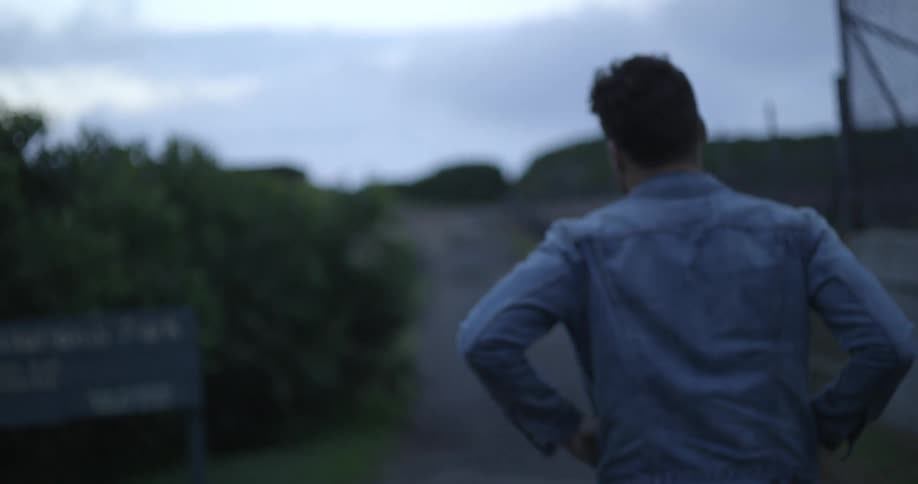 A man in a denim jacket walks on a rural road