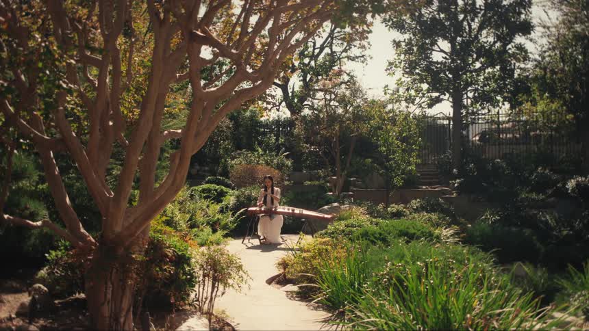 Woman sitting in a green garden and playing a stringed instrument