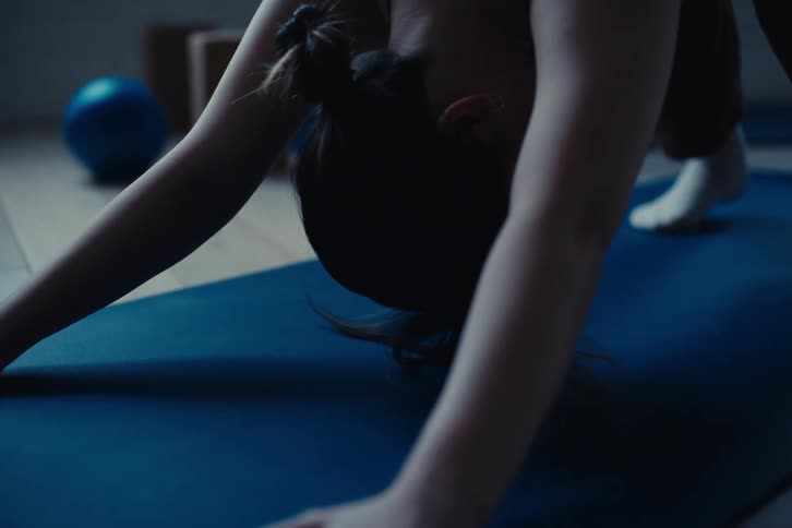 Close up of a woman stretching over a yoga mat in a dimly lit room