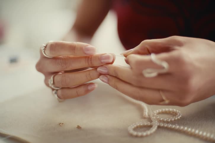 Closeup of a persons hands threading a pearl necklace