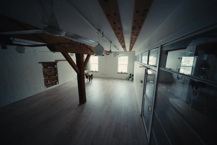 A woman practicing yoga in a spacious minimalist studio with large windows and exposed wooden beams