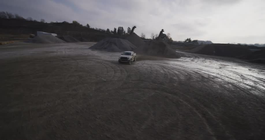 A silver pickup truck driving through a muddy quarry with piles of gravel in the background