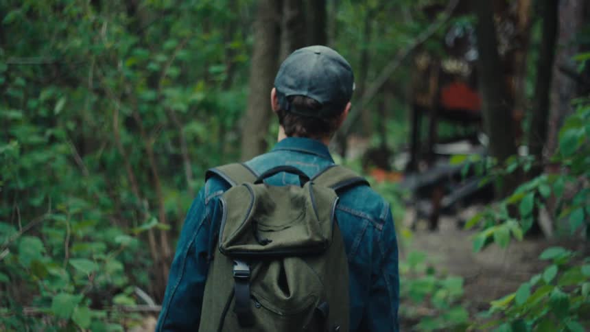 Man hiking through the forest to an abandoned house covered in graffiti