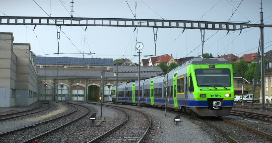 Green and silver train parked over the railroad next to a station surrounded by houses and vegetation outdoors during daytime
