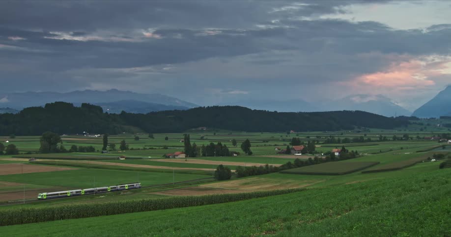 Train passing through the railroad next to a rural area surrounded by vegetation and hills outdoors during daytime