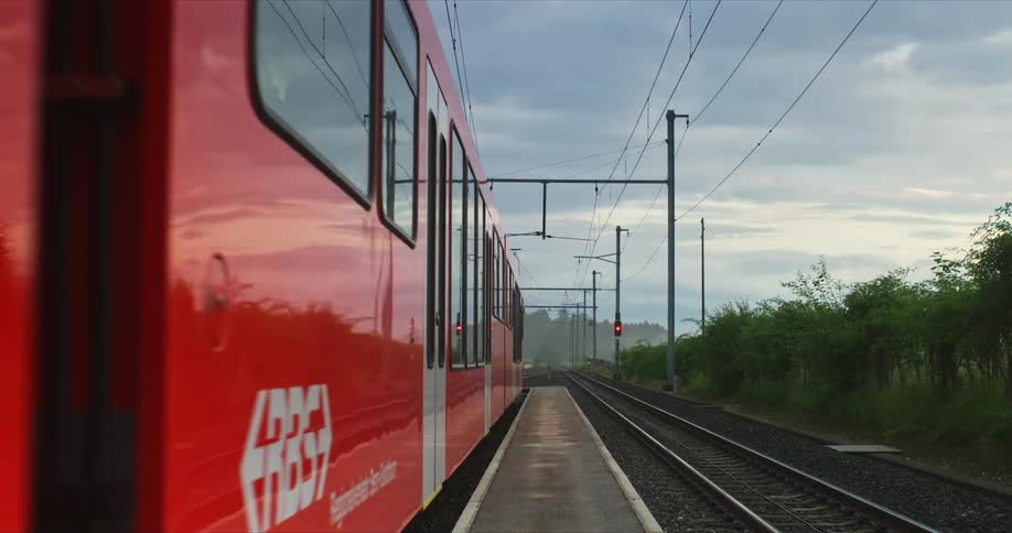 A red train passing over a track next to an empty track surrounded by vegetation with hills and the sky on the background outdoors during daytime