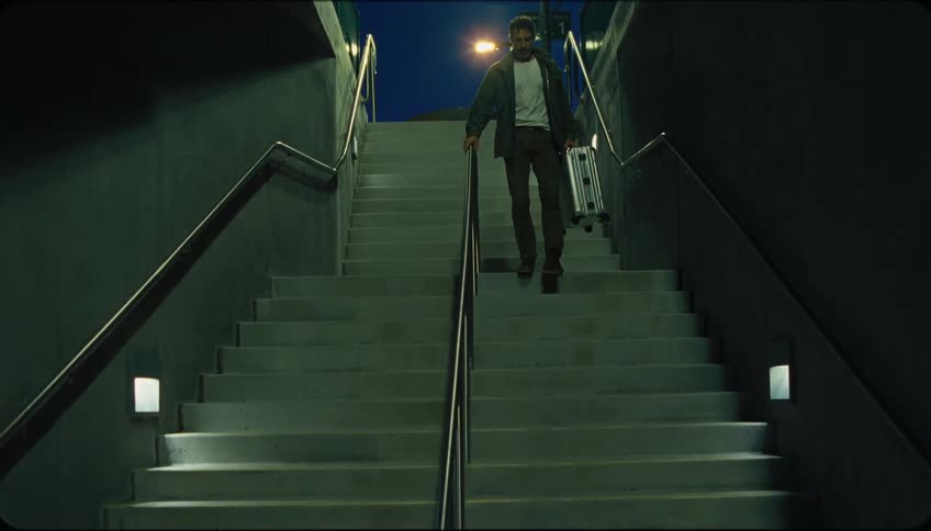 Man walks down a staircase at night while carrying a suitcase