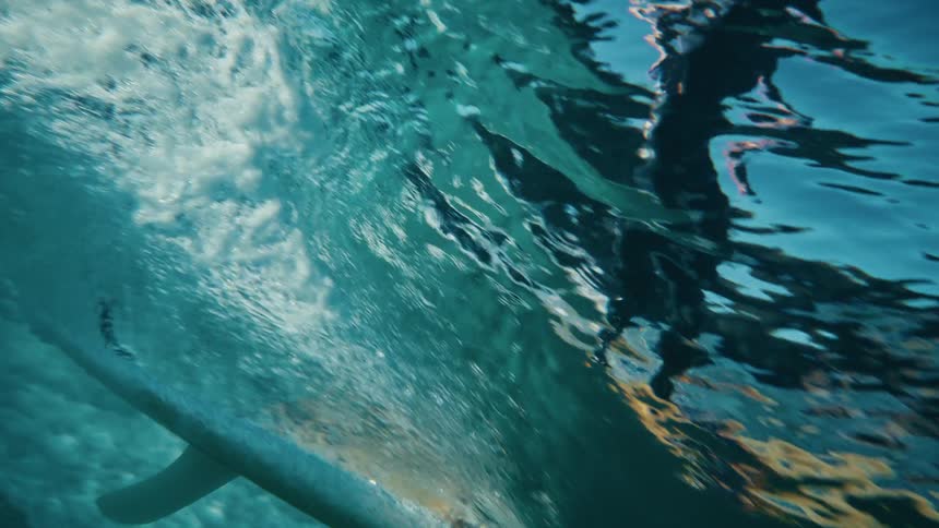 Underwater view of a surfboard cutting through a wave