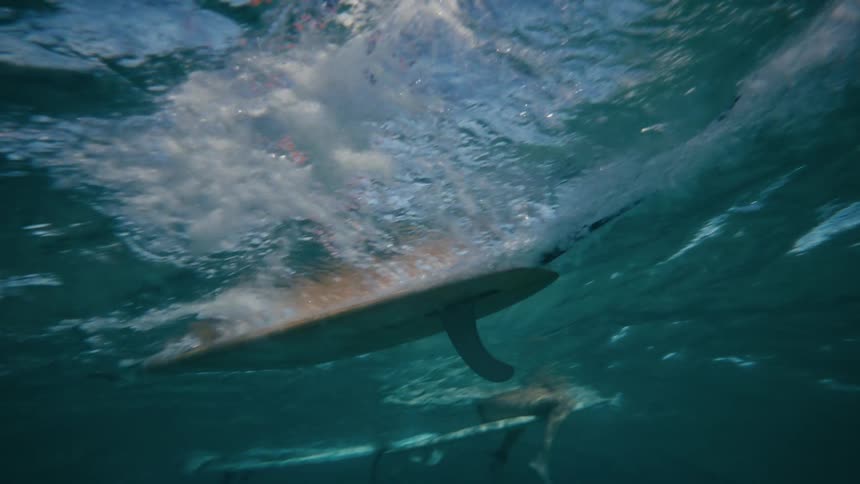 An underwater view of a surfboard with a fin cutting through the water