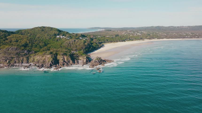A scenic aerial view of a secluded beach with a rocky headland and lush green hills