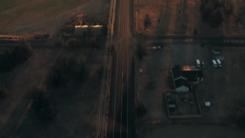 Aerial view of a long highway surrounded by natural fields with a reflection of the sun on the horizon