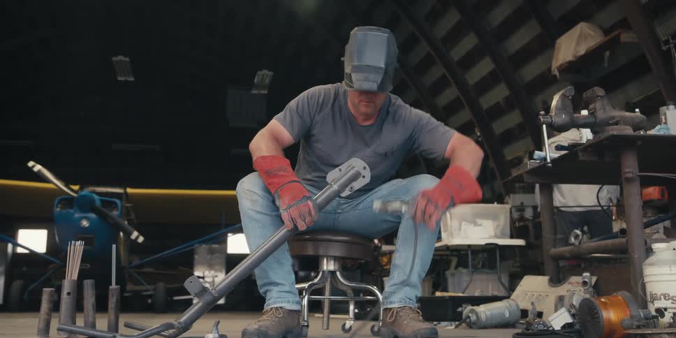 A person in protective gear is handling metal pieces to weld them