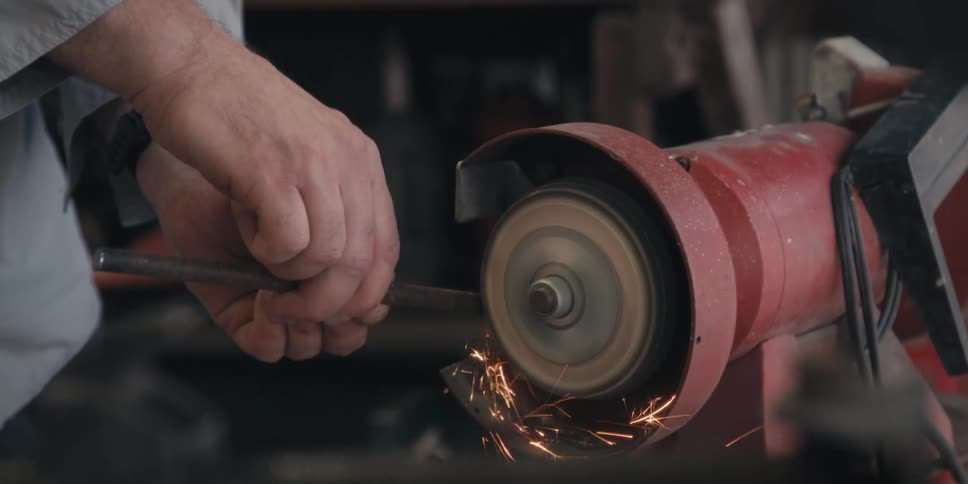 A person using a piece of metal to pass over a tool that is rotating and giving off several sparks on contact