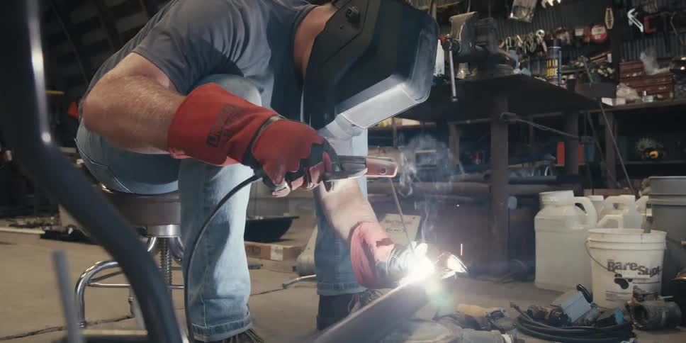 Man with mask and protective glove handling a tool and welding a metal