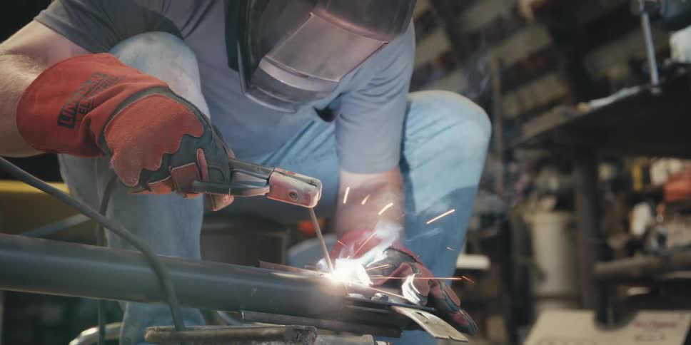 A man wearing a helmet and gloves welding a piece of metal that is giving off several bright sparks