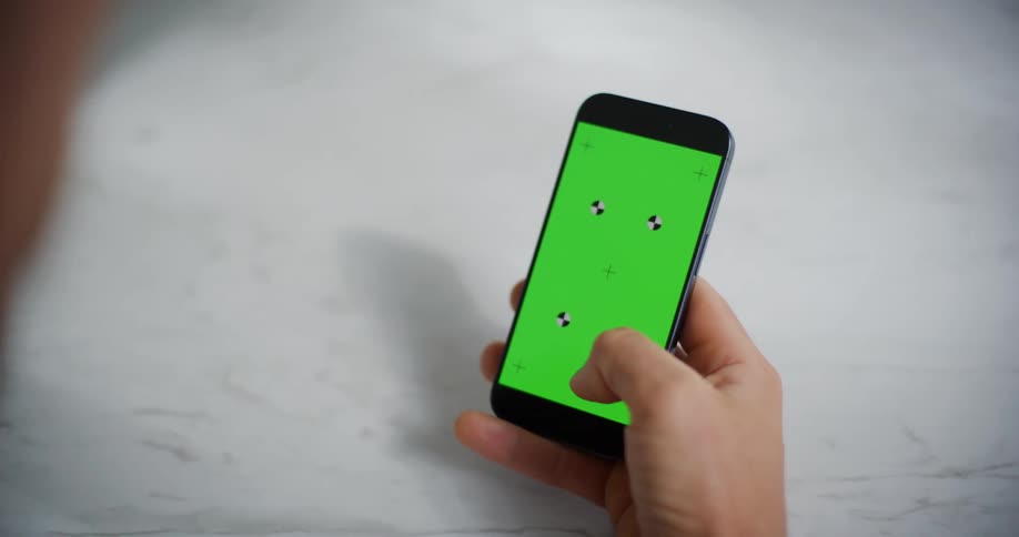 A hand is holding a smartphone with a green screen displaying four tracking markers