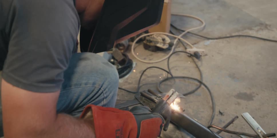 A person in protective gear is welding metal pieces together with bright sparks flying