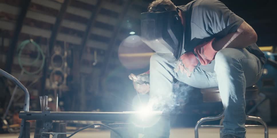 A person in protective gear is welding metal pieces together with bright sparks flying