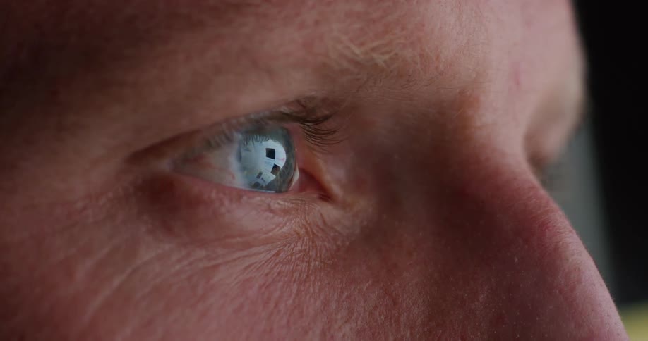 A persons eye with a blue iris with images reflecting on the surface of the eye and it is moving sideways