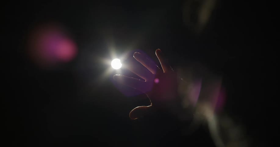 A person placing his hand in front of a white light coming from the sky that is completely dark