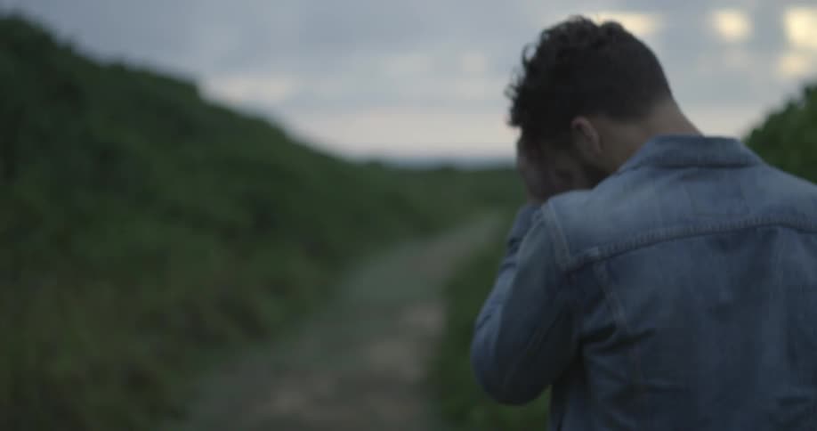 A man walking along a dirt path between hills on a cloudy day