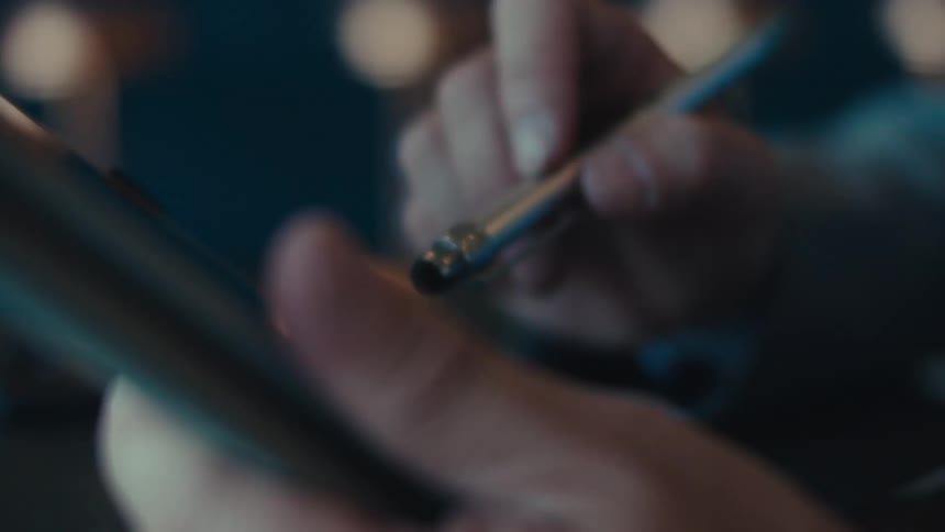 A hand using a stylus pen to interact with a tablet device