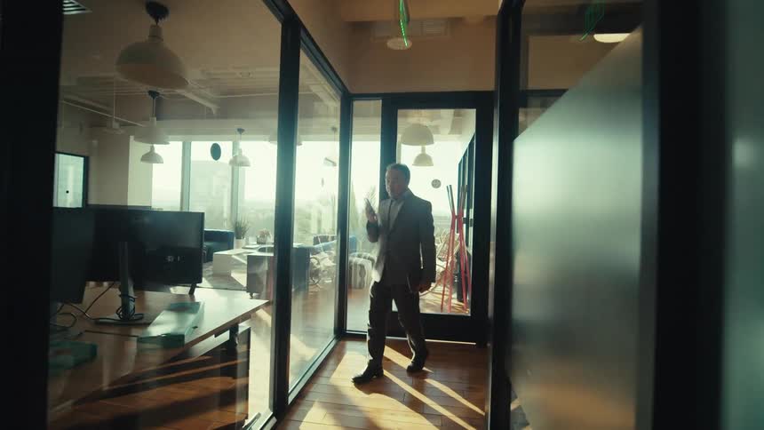 Man walking down an office hallway answering a phone call