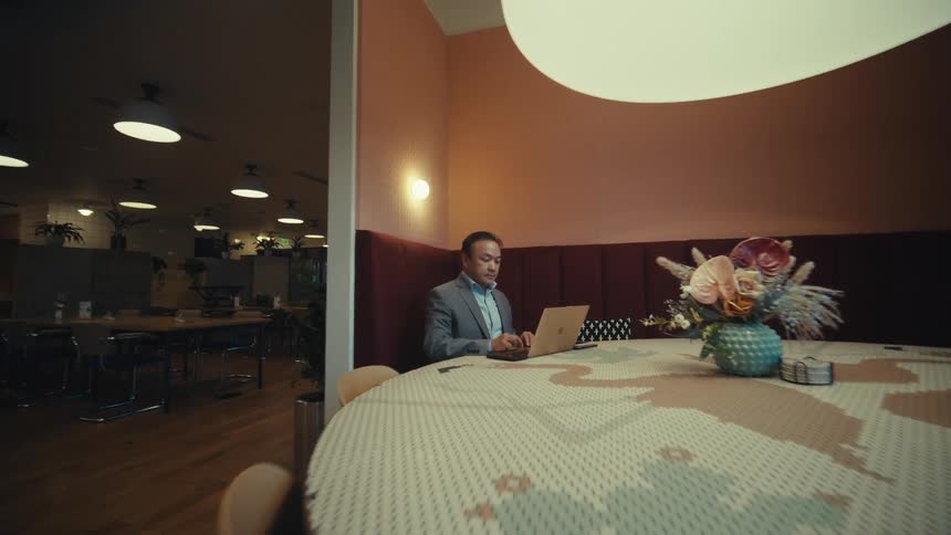 A man sitting at a large round table in a modern restaurantworking on a laptop