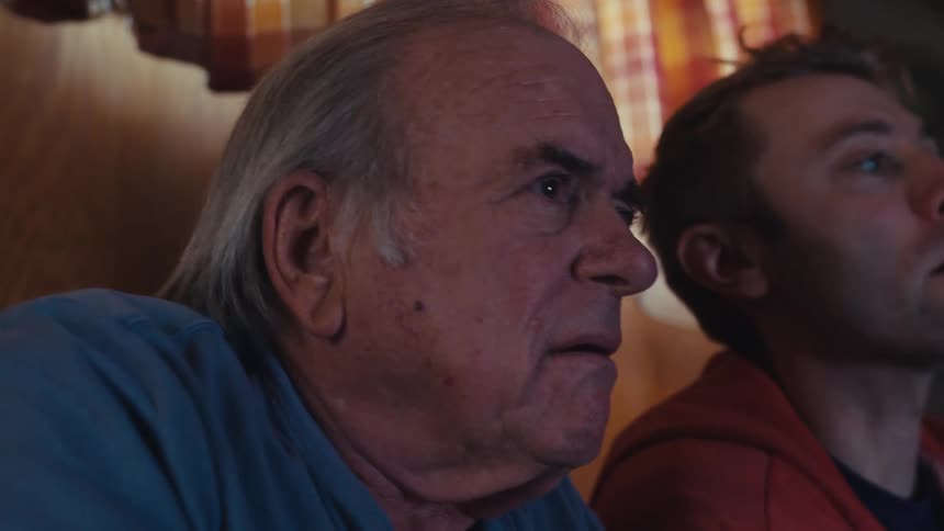 Father and son are sitting in a dimly lit living room playing video games together