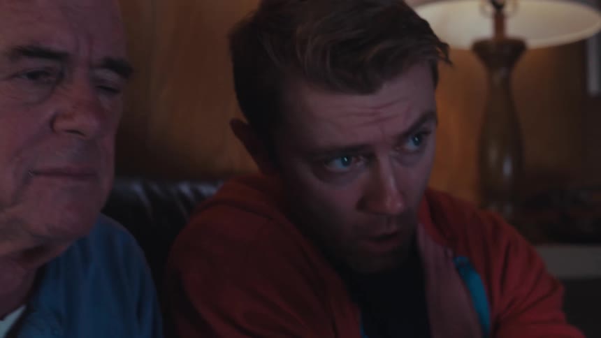 A man concentrates intently while listening to his son explaining something to him as they sit in a dimly lit living room