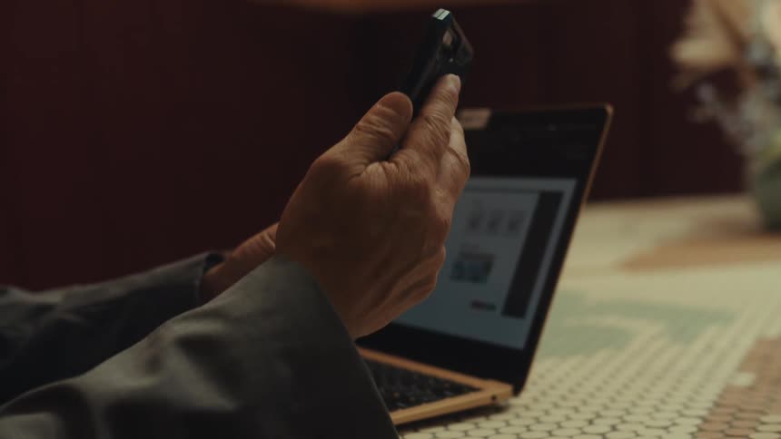 A man is shown working on a laptop before picking up a phone then looking downward with a close up of his profile