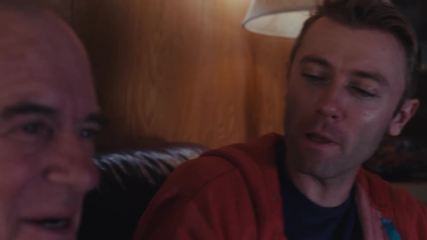 Father and son are sitting in a dimly lit living room having a lively conversation while watching tv