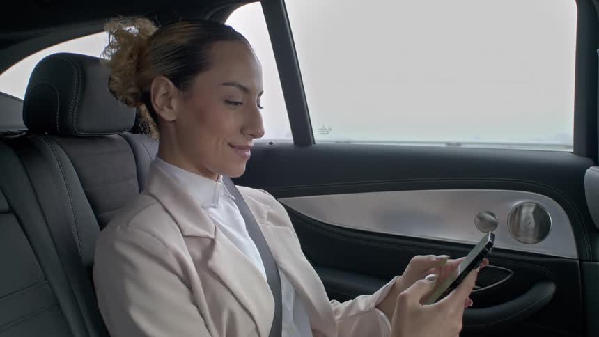Formally dressed female passenger riding in a car smiles while texting on her smartphone