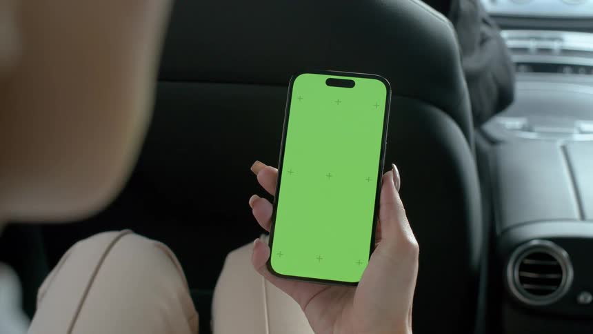 A person is holding a smartphone with a green screen while sitting in the backseat of a car
