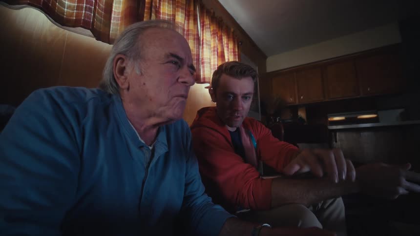 A young man explains to his elderly father how to use video game controls while playing together at home