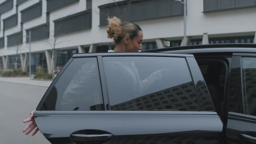 A woman boards a black taxi on a street lined with modern office buildings