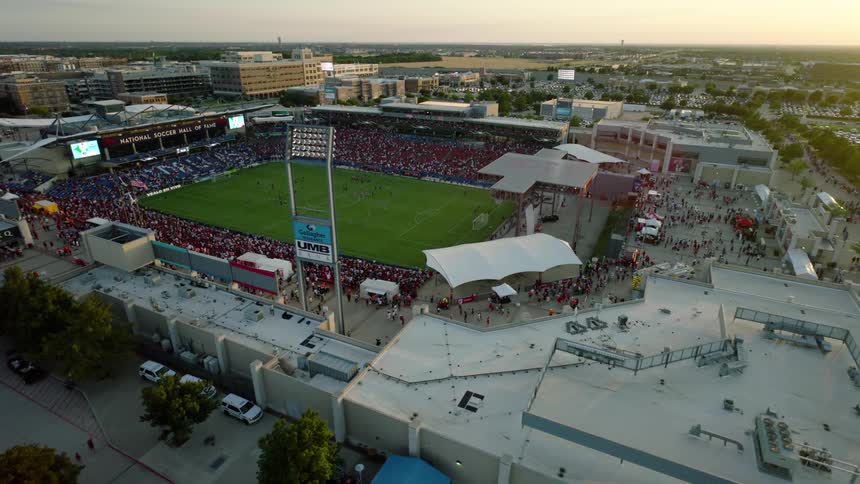 A packed stadium surrounded by city buildings and parking lots with crowds milling outside before a game