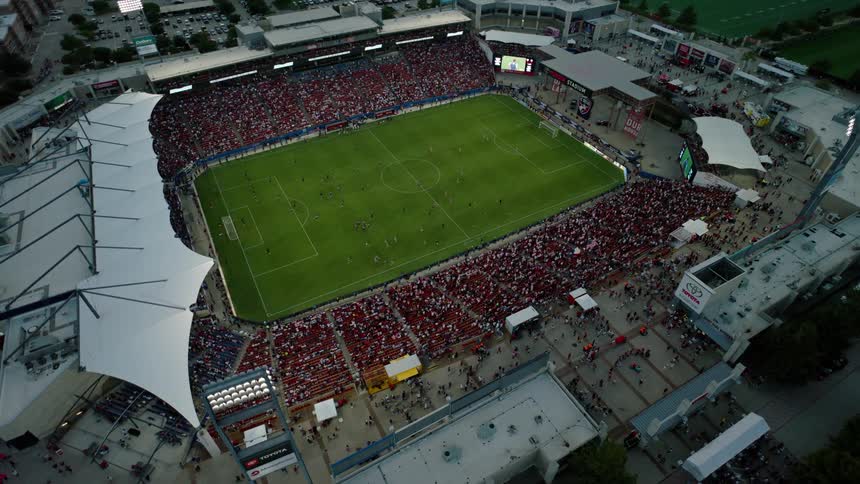 An aerial view of a packed soccer stadium during a match with a vibrant crowd filling the stands