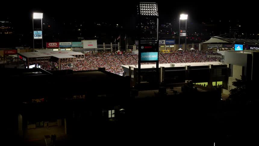 An outdoor sports stadium is illuminated at night with the stands packed with spectators