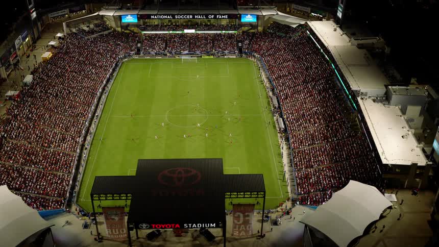 An aerial view of a packed soccer stadium during a match with a large crowd filling the stands