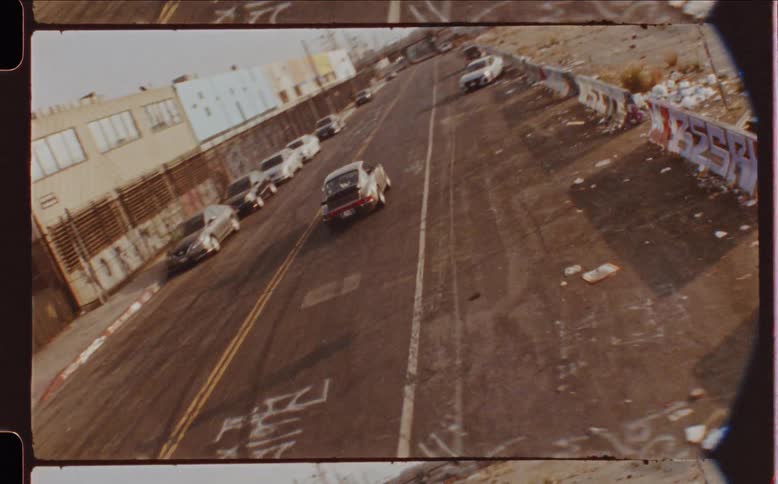 A grainy vintagestyle shot captures a single car driving down a city street
